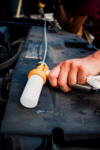 Image of an empty oil sample bottle attached to a pump with tubing threaded into the dipstick in an engine