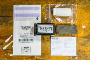 A free oil sample kit from Blackstone with all the components spread out: a white bottle, black mailer, return envelope, gray absorbent material, ziplock bag, and instructions
