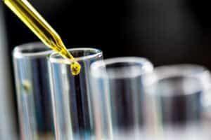 An eye dropper putting a drop of fresh engine oil into a clean test tube.