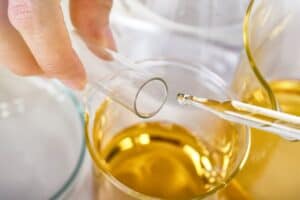 Close-up of a dropper putting a drop of oil into a test tube above a beaker of oil