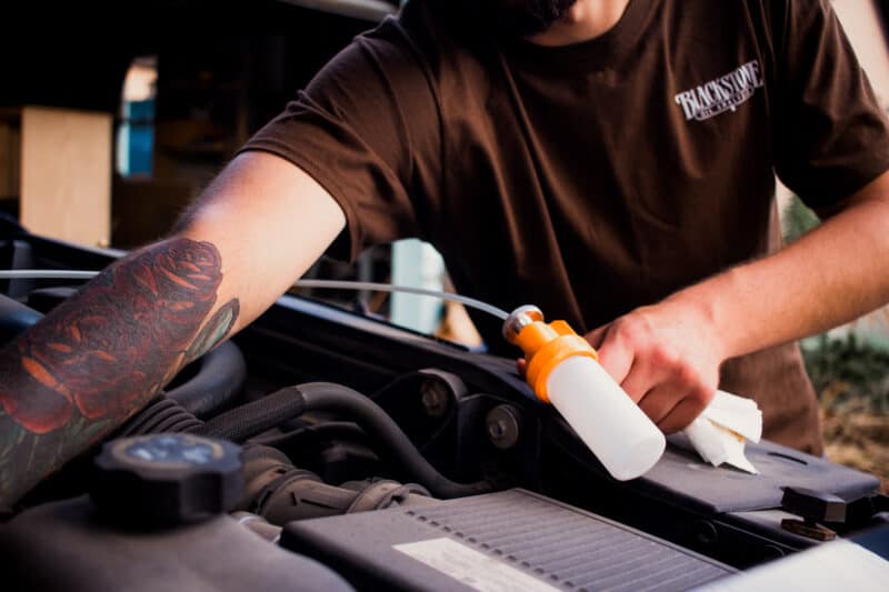 Tattooed arm reaching into an engine with a sampling pump and tubing